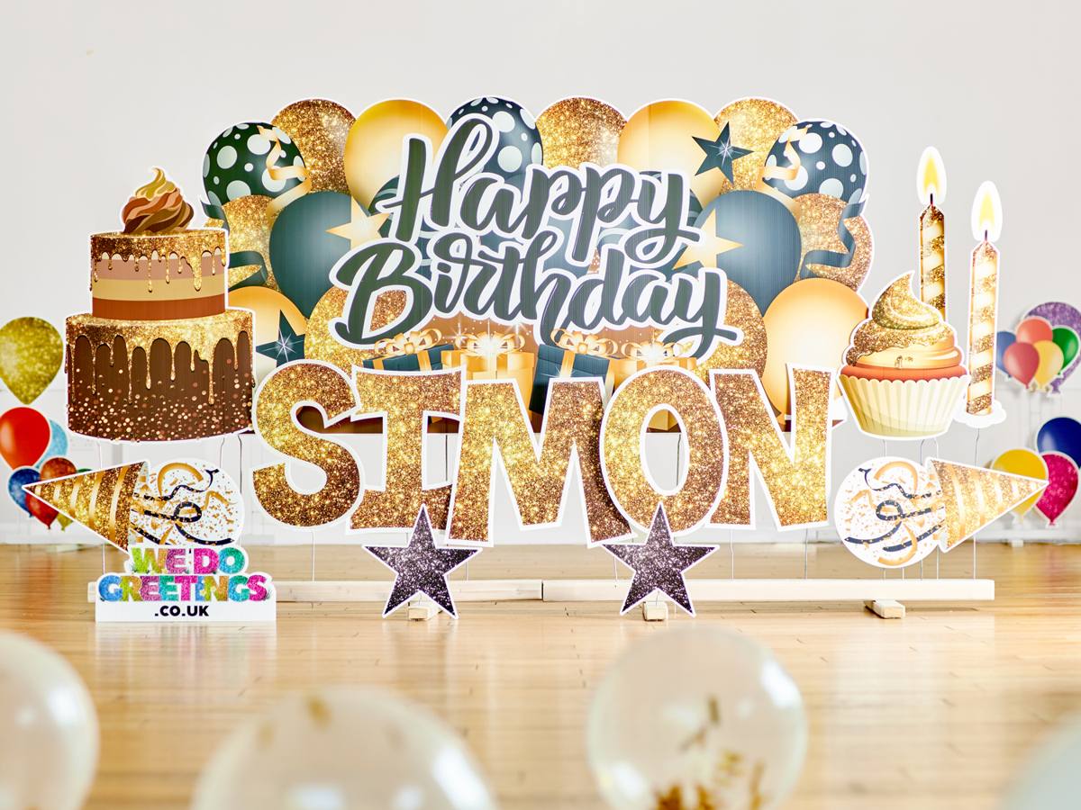 Happy Birthday Simon in gold glitter letters with a cake and balloon backdrop on the plinth stand in a living room