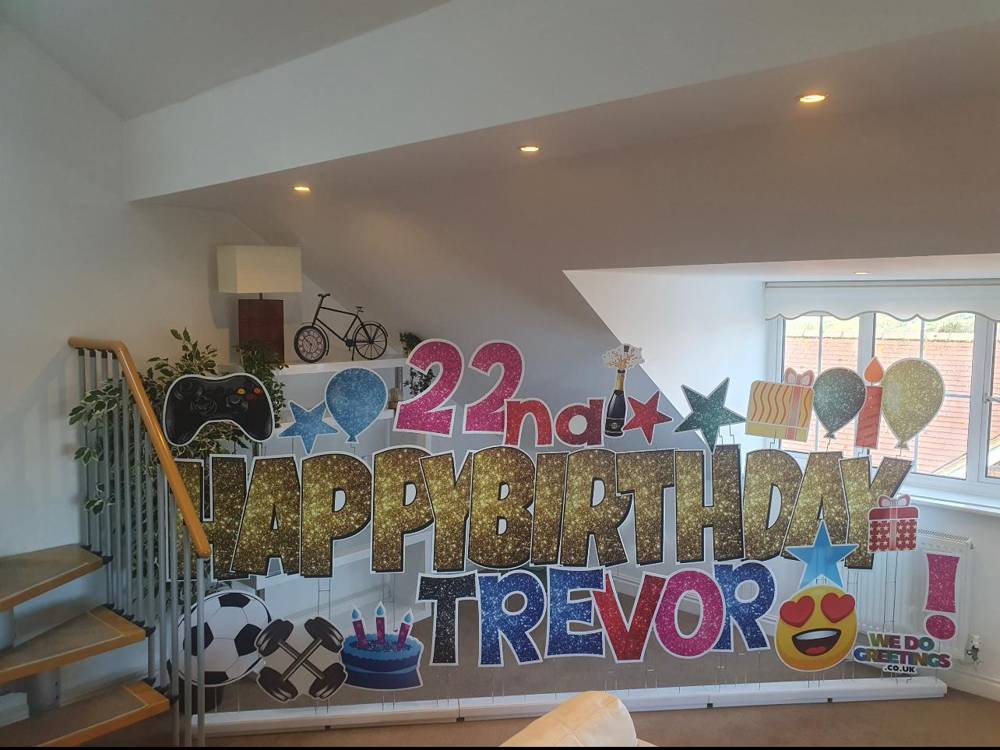 Happy 22nd Birthday Trevor in gold glitter letters filling a loft room, candles and cake accessories