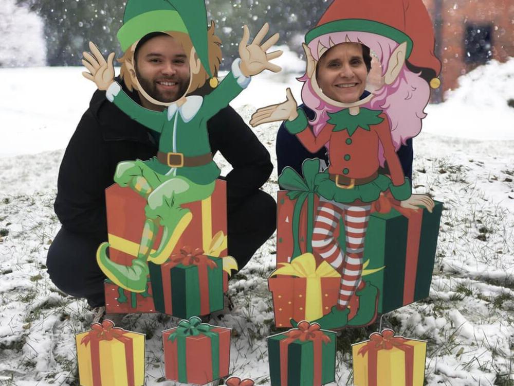 Two people with their faces through the elf photo boards in the snow
