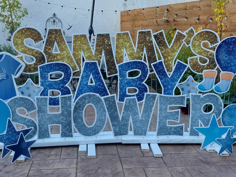 Sammy's Baby Shower in gold, blue and silver glitter letters on a patio