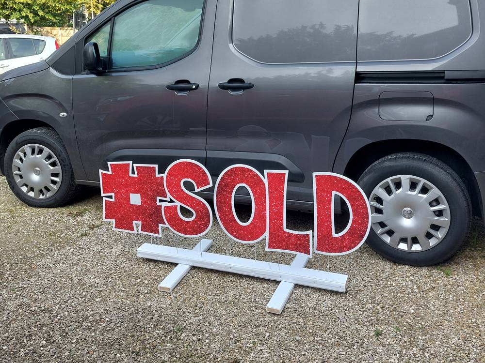 #SOLD in red glitter letters beside a grey van