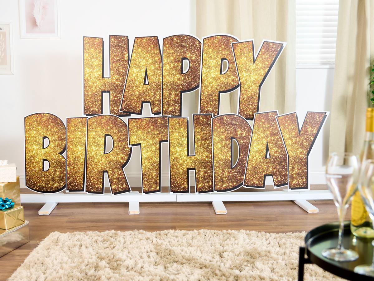 Oversized gold glitter letters spelling HAPPY BIRTHDAY on the plinth stand in a living room