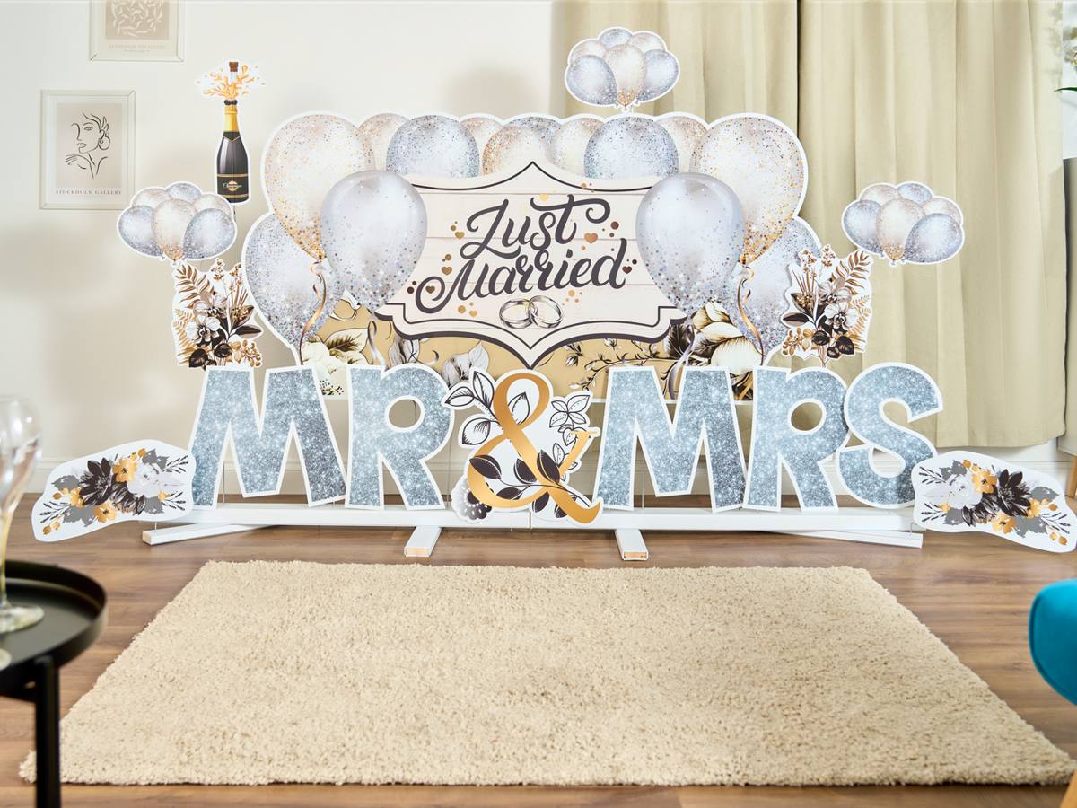 MR & MRS in silver glitter letters with a Just Married balloon backdrop, standing on the white plinth stand on a wooden floor