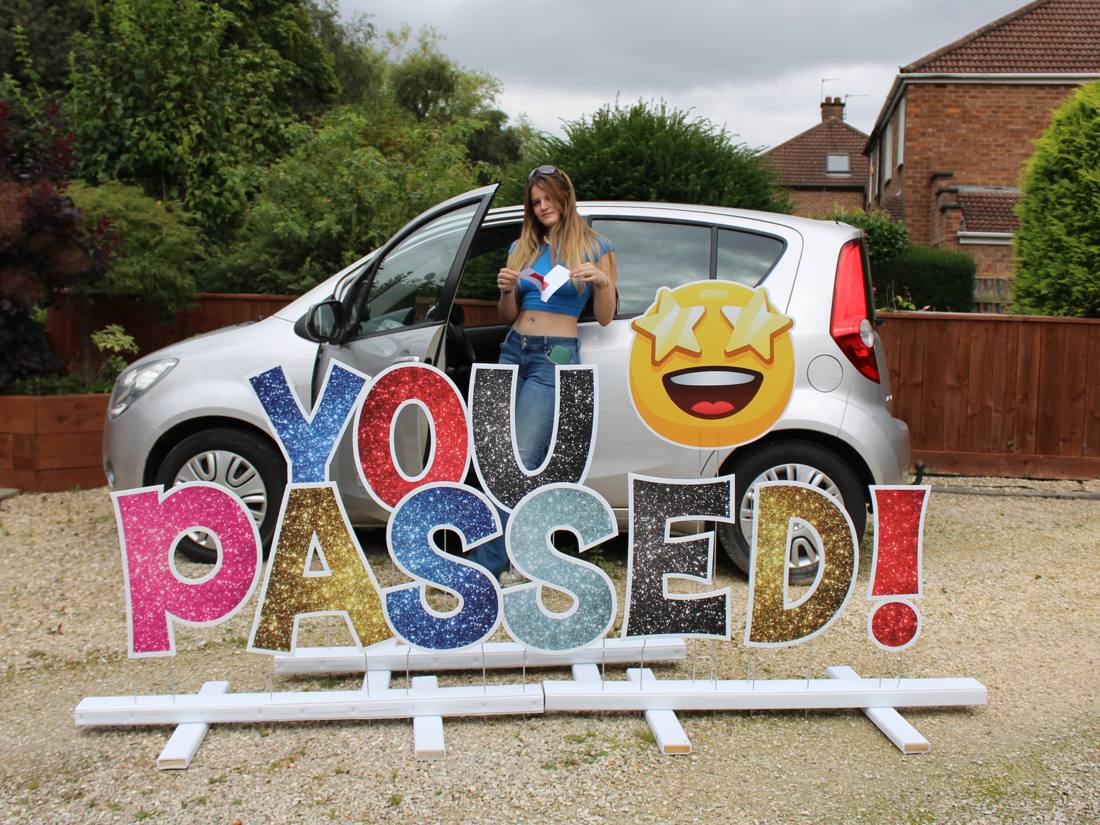 You Passed! letters beside a car with a smiling driver